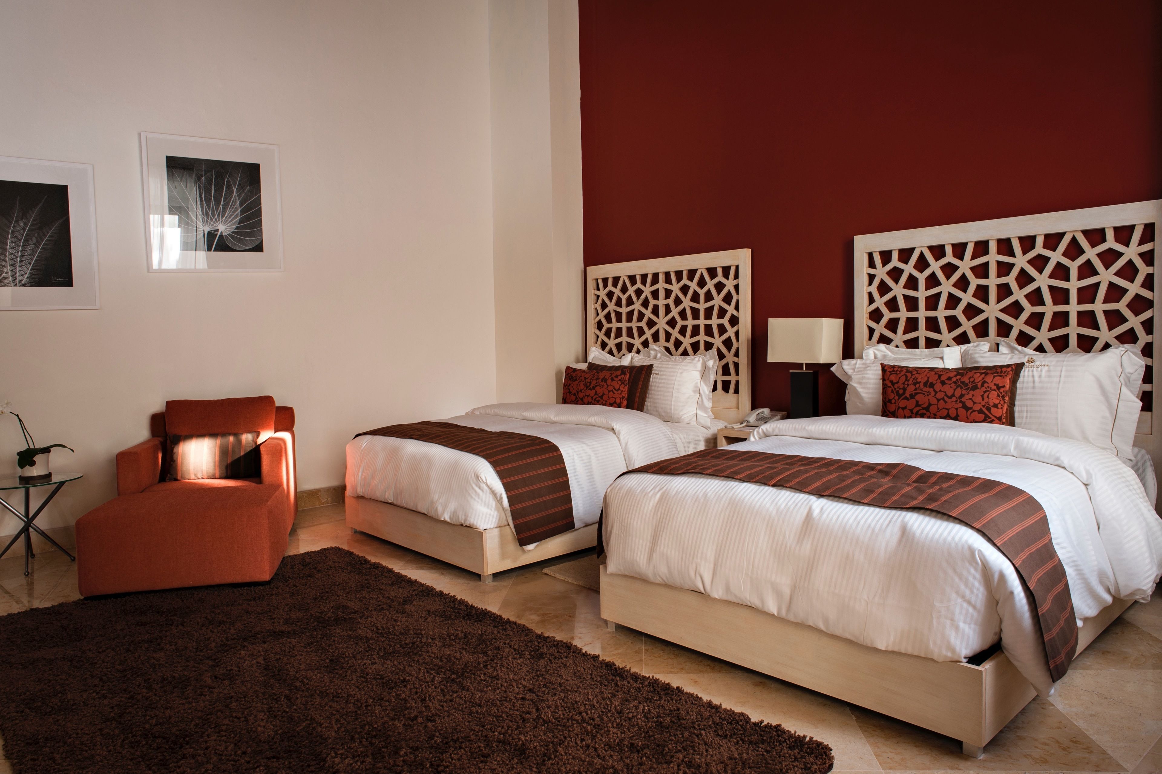 Una habitación de hotel con dos camas, una pared de acento roja y una alfombra marrón.