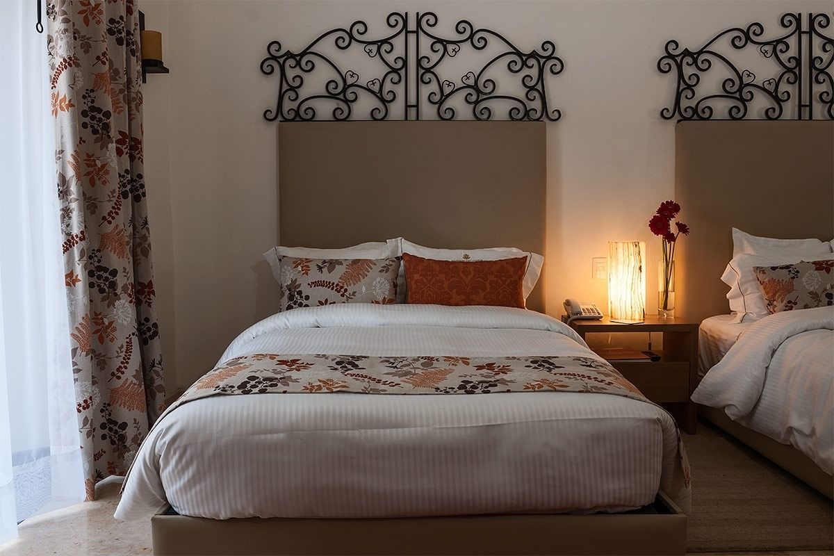 Una cama doble con colcha estampada de flores, una mesita de noche con lámpara y un cabecero decorativo de metal.