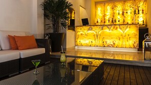Un coin bar doté d’un comptoir en marbre, d’un canapé avec des coussins orange et d’une table en verre sur laquelle repose un verre à martini.