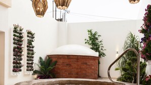 Un bain à remous avec un intérieur carrelé, entouré de meubles en osier et agrémenté d’un magazine posé sur un coussin.