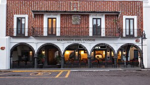 Un bâtiment à la façade recouverte de tuiles, doté d’entrées en arc de cercle et d’une enseigne indiquant : « MANSIÓN DEL CONDE HOTEL BOUTIQUE & SPA ».