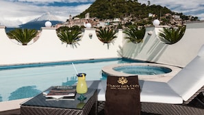 Un espace piscine avec des chaises longues, un jacuzzi et une vue sur la montagne et la ville.