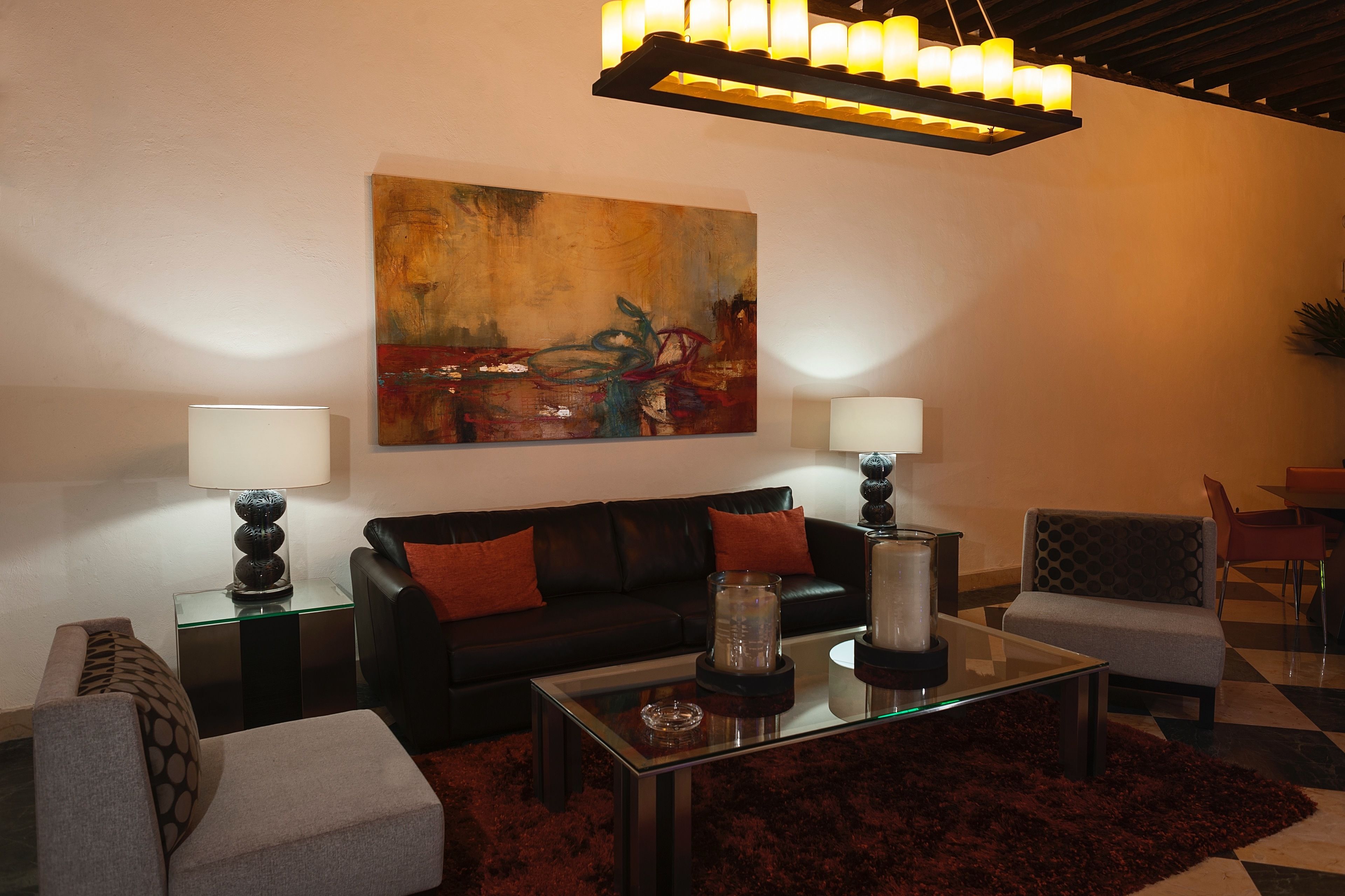Una sala moderna con un sofá de cuero negro, dos mesitas de noche con lámparas, una mesa de centro de vidrio y un cuadro abstracto grande en la pared.