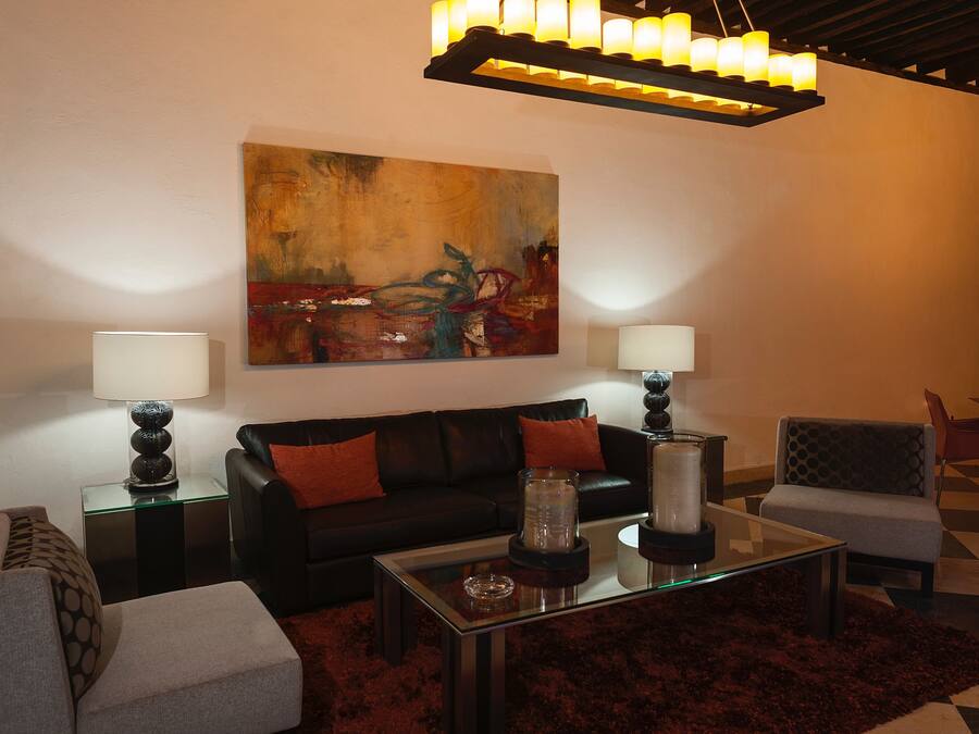 Una sala moderna con un sofá de cuero negro, dos mesitas de noche con lámparas, una mesa de centro de vidrio y un cuadro abstracto grande en la pared.