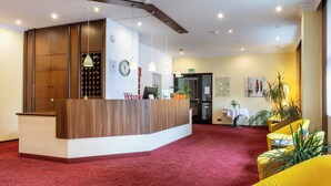 A reception area with a wooden reception desk, a red carpet, and yellow chairs. - Montana Hotel Mönchengladbach (Moenchengladbach)