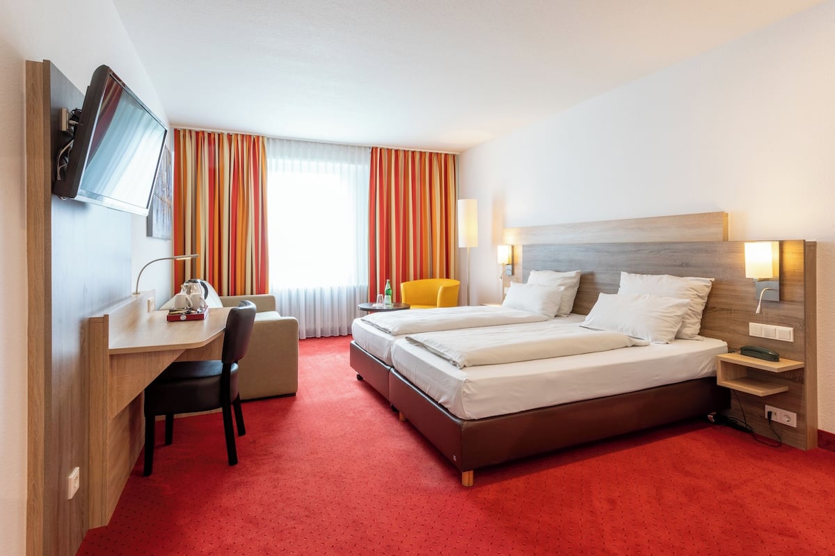 A hotel room with a bed, a desk, a chair, a TV, and a window with curtains.