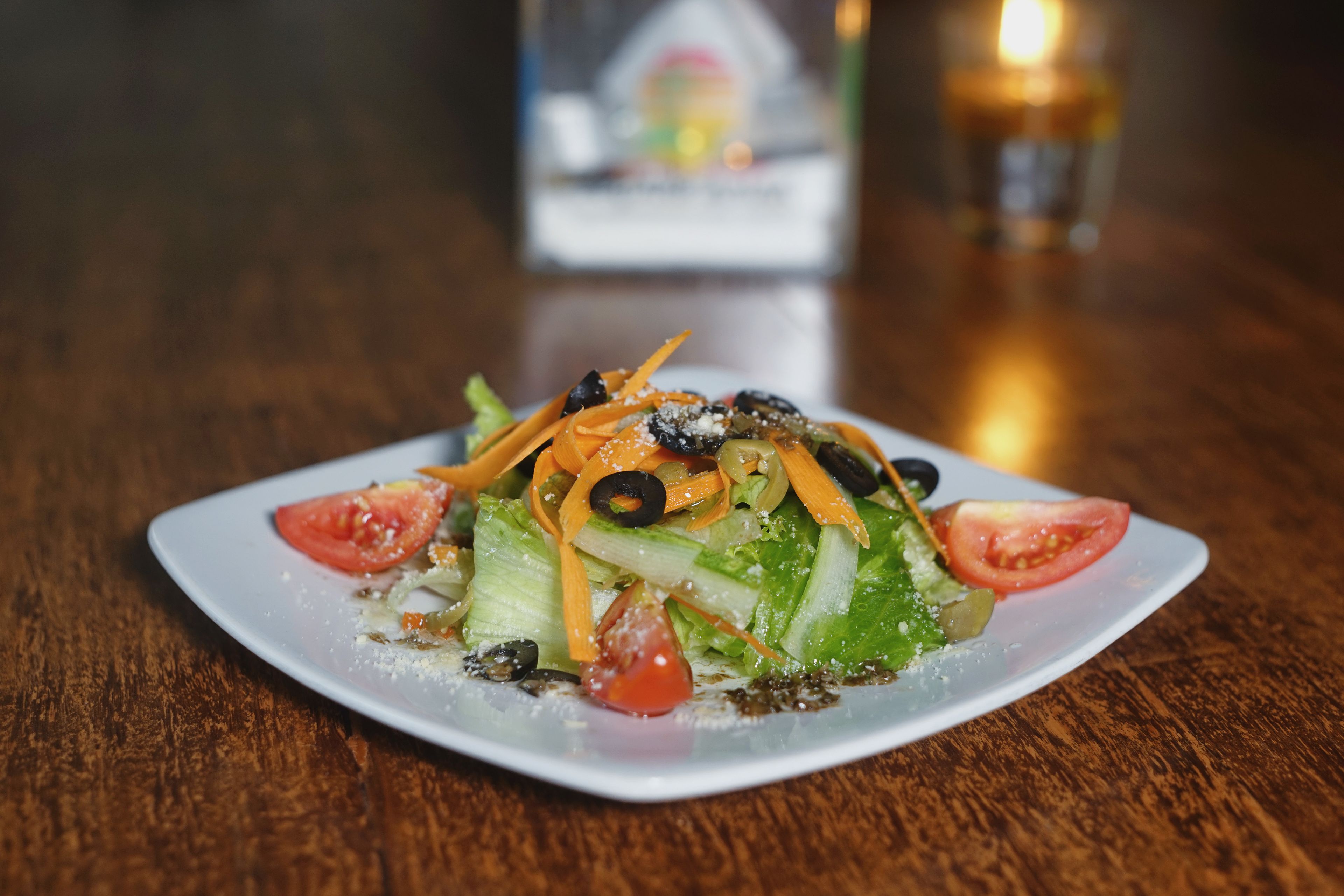 A square white plate with a salad on a wooden table.