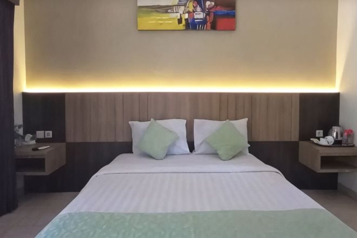 Una habitación de hotel con una cama grande, dos mesitas de noche y un cuadro en la pared.