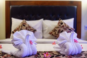 A bed with two towels shaped like swans, a floral-patterned bedspread, and a dark upholstered headboard. - Segara Anak Hotel (Kuta)