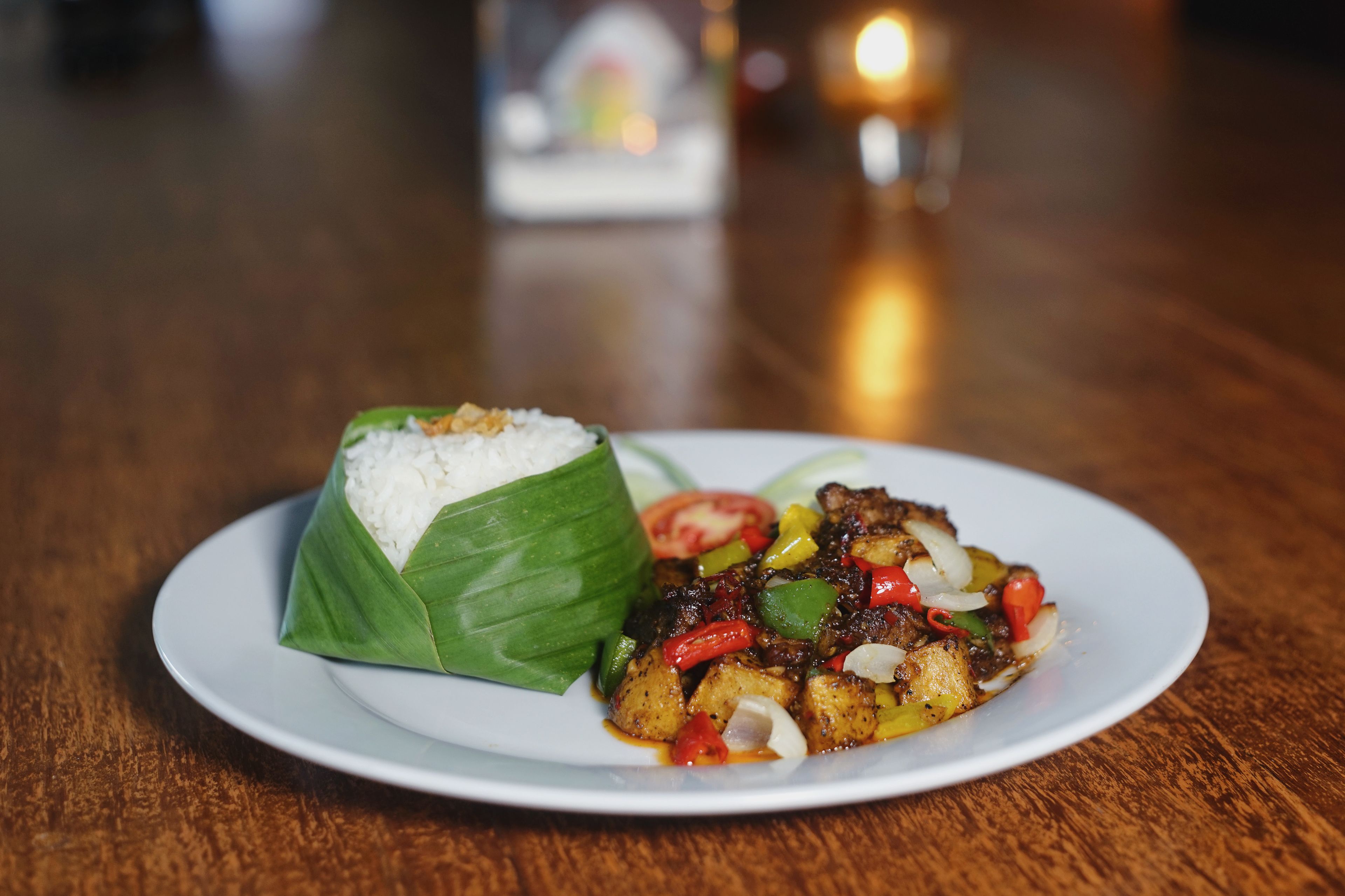 A plate of food with rice wrapped in banana leaves and a stir-fry dish.