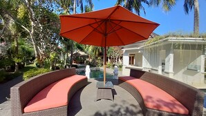 Un espace aménagé au bord de la piscine, avec des meubles en osier et un parasol rouge.