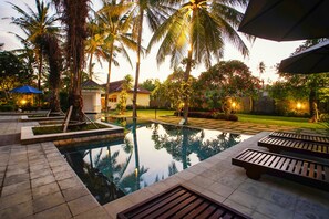 A pool area with wooden loungers, palm trees, and a well-maintained lawn. - Segara Anak Hotel (Kuta)