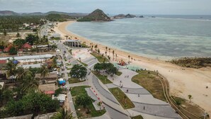 Une zone côtière comprenant une plage, une promenade et une petite colline en arrière-plan.