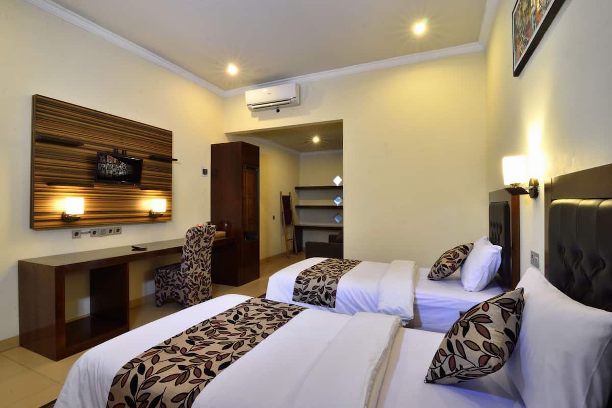 Habitación de hotel con dos camas, un escritorio, una silla y un televisor montado en la pared.