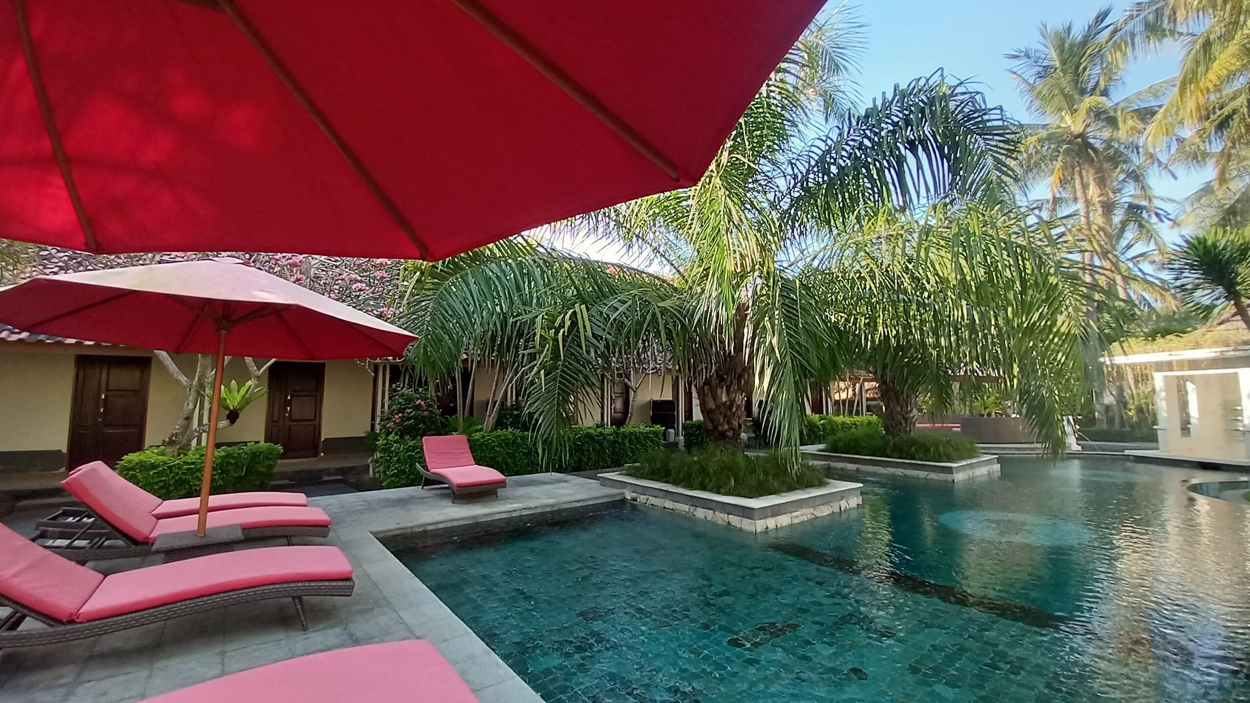 A pool area with lounge chairs and a red umbrella.