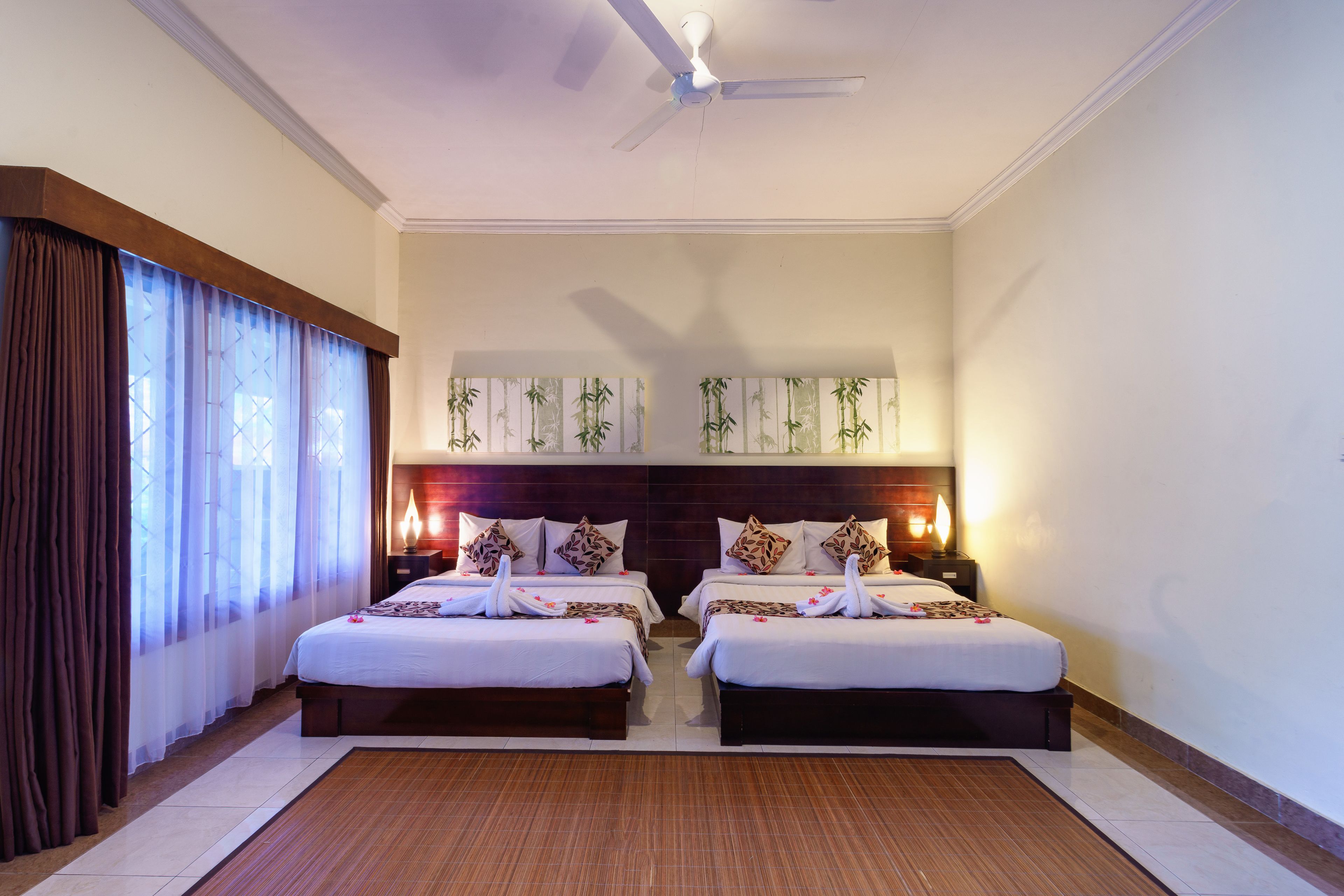 A hotel room with two beds, a ceiling fan, and wall-mounted lamps.