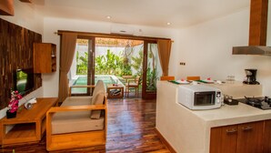 A modern kitchen with a microwave, stove, and dining area. A pool is visible through the glass doors. - Delu Villas Suite Seminyak (Seminyak)