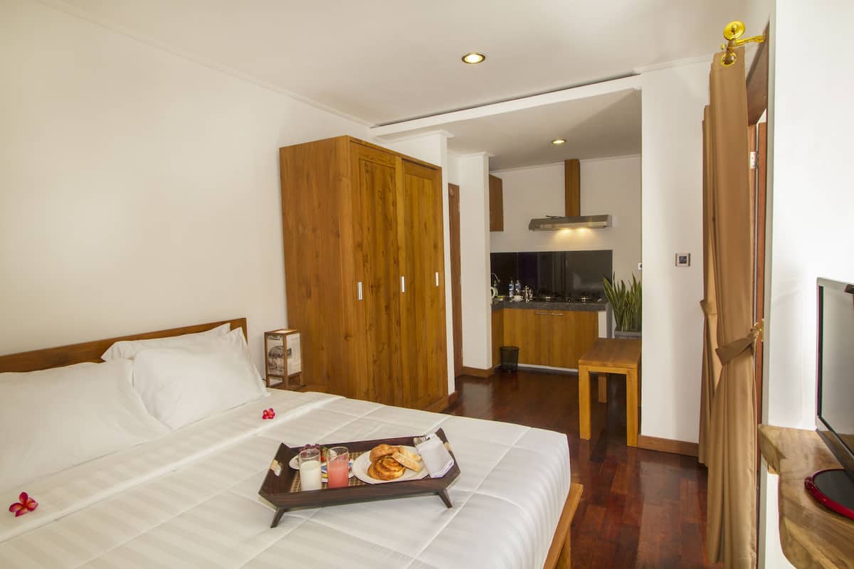 A hotel room with a bed, wooden wardrobe, kitchenette, and a dining area.
