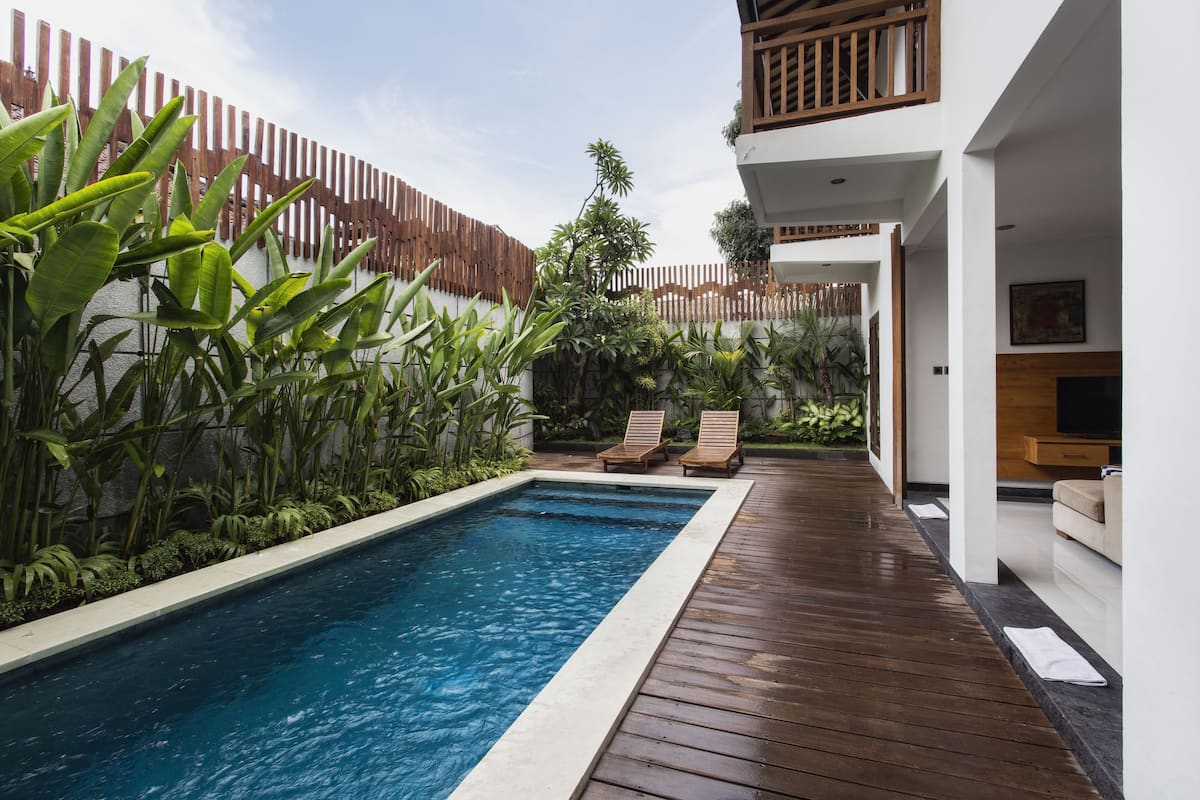 A rectangular swimming pool with a wooden deck surrounding it, two lounge chairs, and a wooden fence.