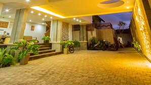 A well-lit outdoor area with a paved walkway, steps leading to a covered entrance, and potted plants. - Delu Villas Suite Seminyak (Seminyak)