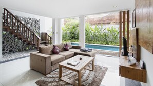 A modern living room with a beige sofa, a wooden coffee table, and a pool view. - Delu Villas Suite Seminyak (Seminyak)