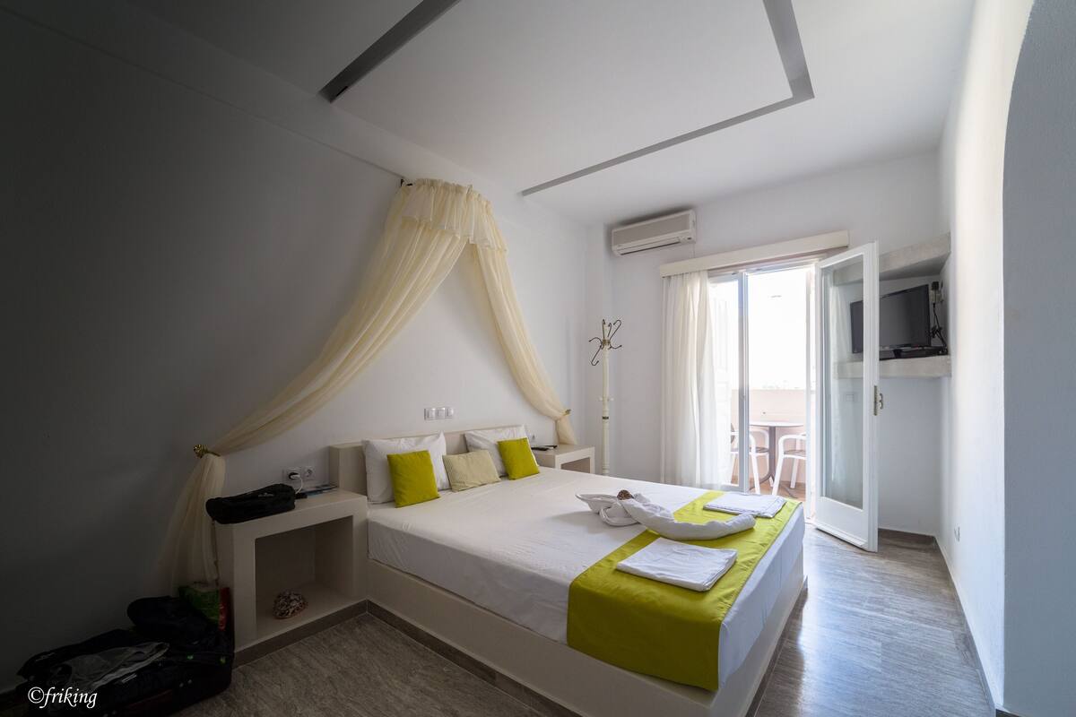 Un dormitorio con cama, mesita de noche, maleta y ventana con cortinas.