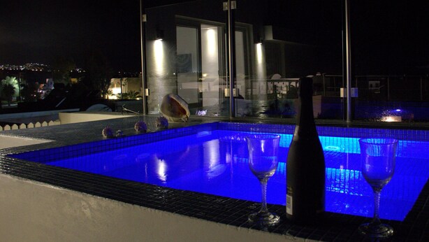Una piscina con barrera de cristal, dos copas de vino y una botella.