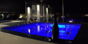 A swimming pool with a glass barrier, two wine glasses, and a bottle of wine. - Argiris Studios (Santorini)