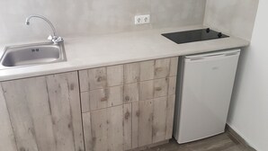 Una cocina compacta con un lavamanos, lavavajillas y placa de inducción negra.