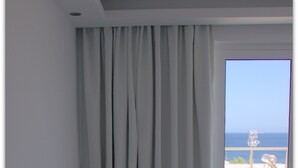 Una habitación con una cama blanca, un ventanal con vista al mar y una cortina.