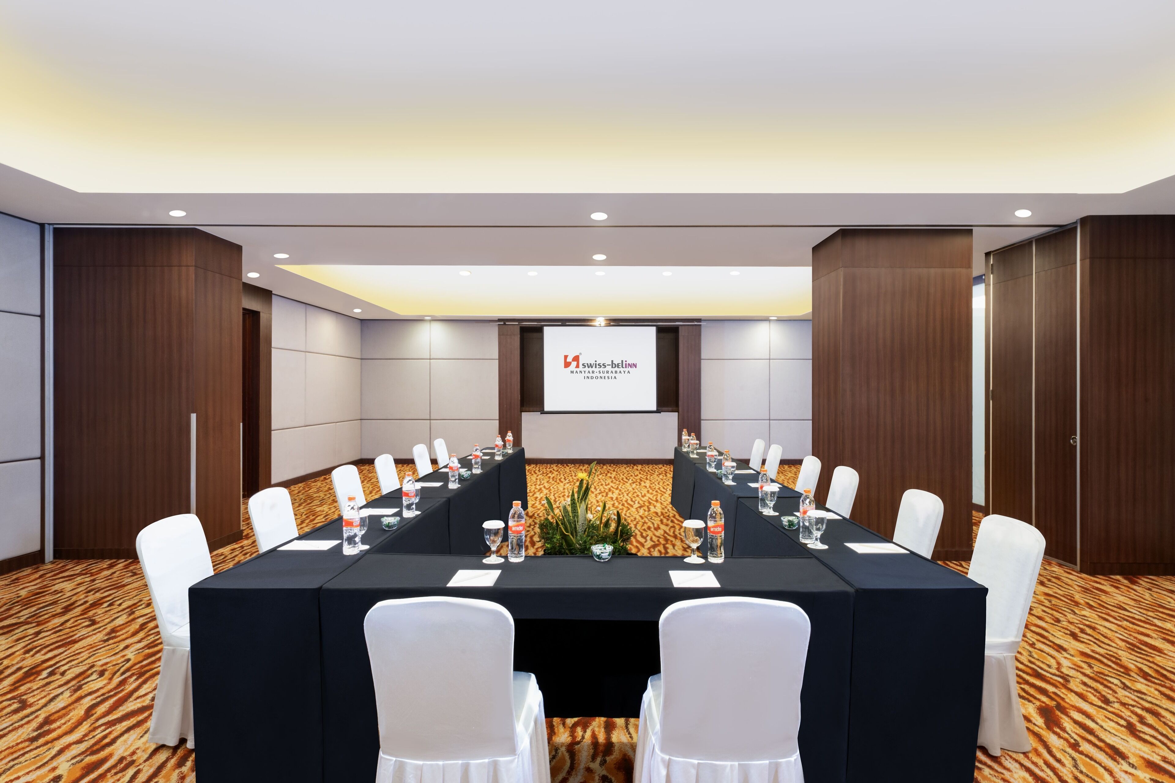 Une salle de conférence avec une longue table, des chaises blanches et un écran de projection sur lequel est affiché le logo de Swiss-Bellinn.