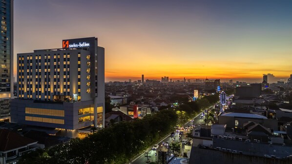 Un hotel de gran altura con un llamativo letrero 'Swiss-Bellinn', rodeado por un paisaje urbano al atardecer.