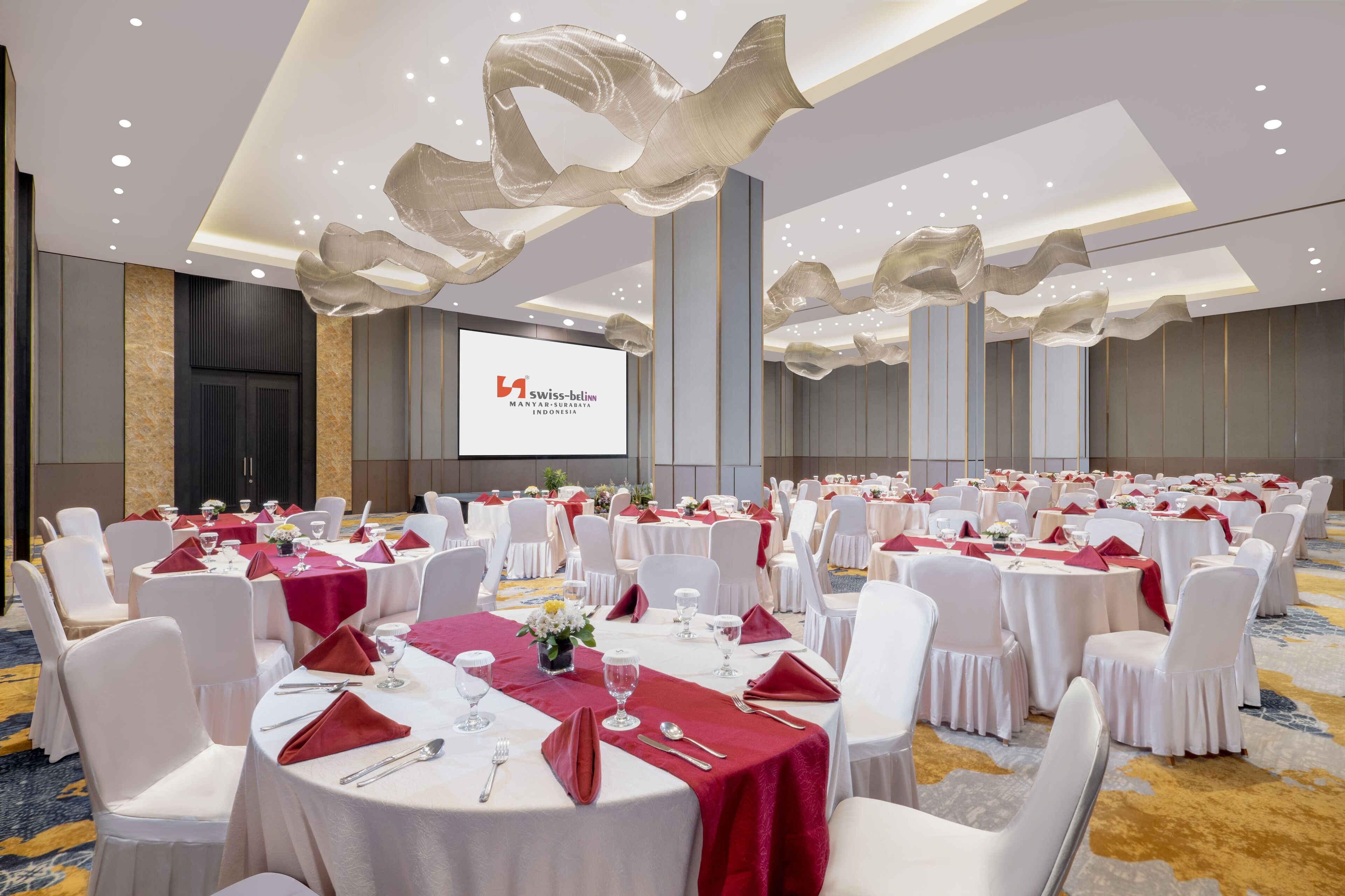 A banquet hall with round tables, white chairs, and red tablecloths.