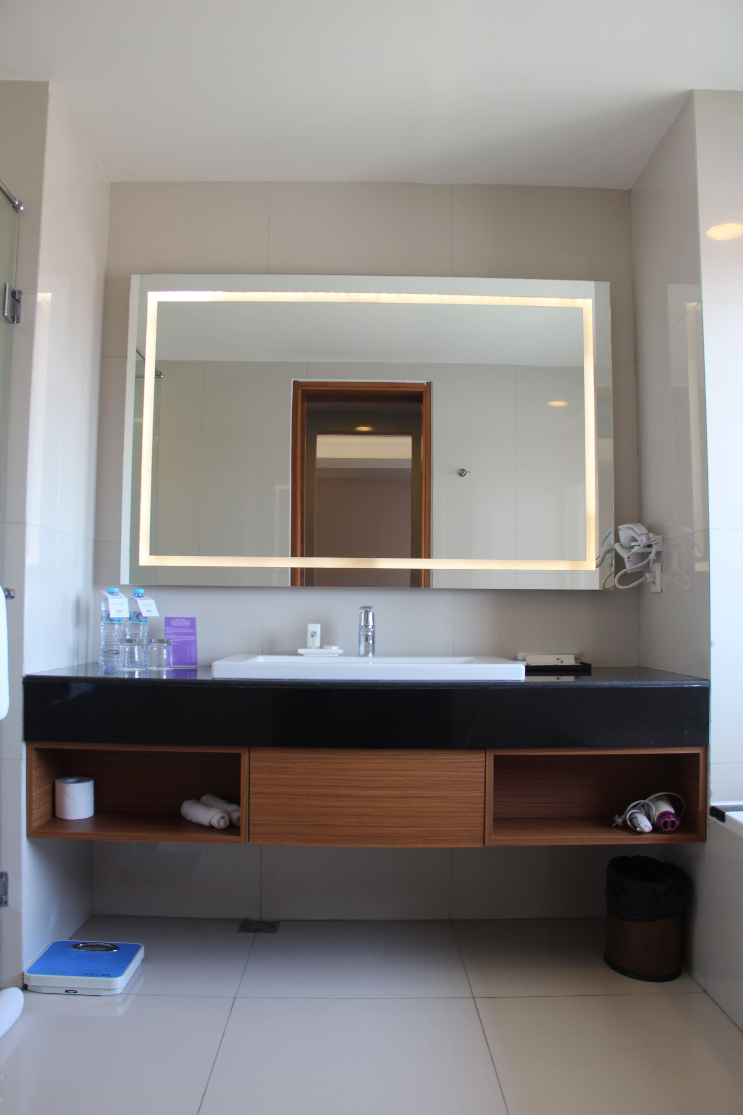 Une salle de bain moderne avec un grand miroir, un lavabo blanc et des étagères en bois.