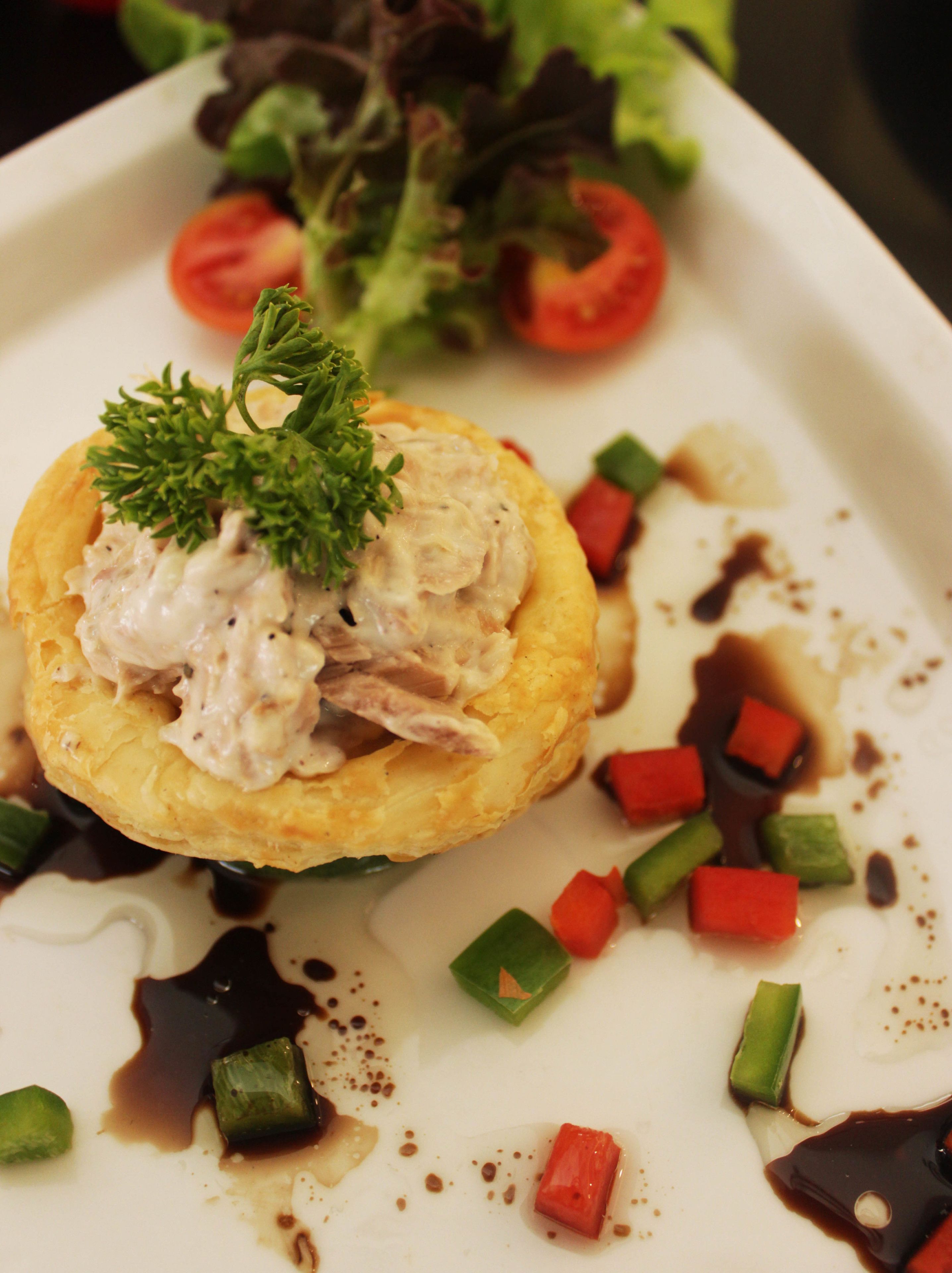 Un plato con un pastel horneado cubierto de crema, adornado con perejil, rodeado de vegetales picados y salsa.