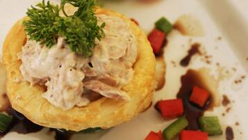 Un plato con un pastel horneado cubierto de crema, adornado con perejil, rodeado de vegetales picados y salsa.