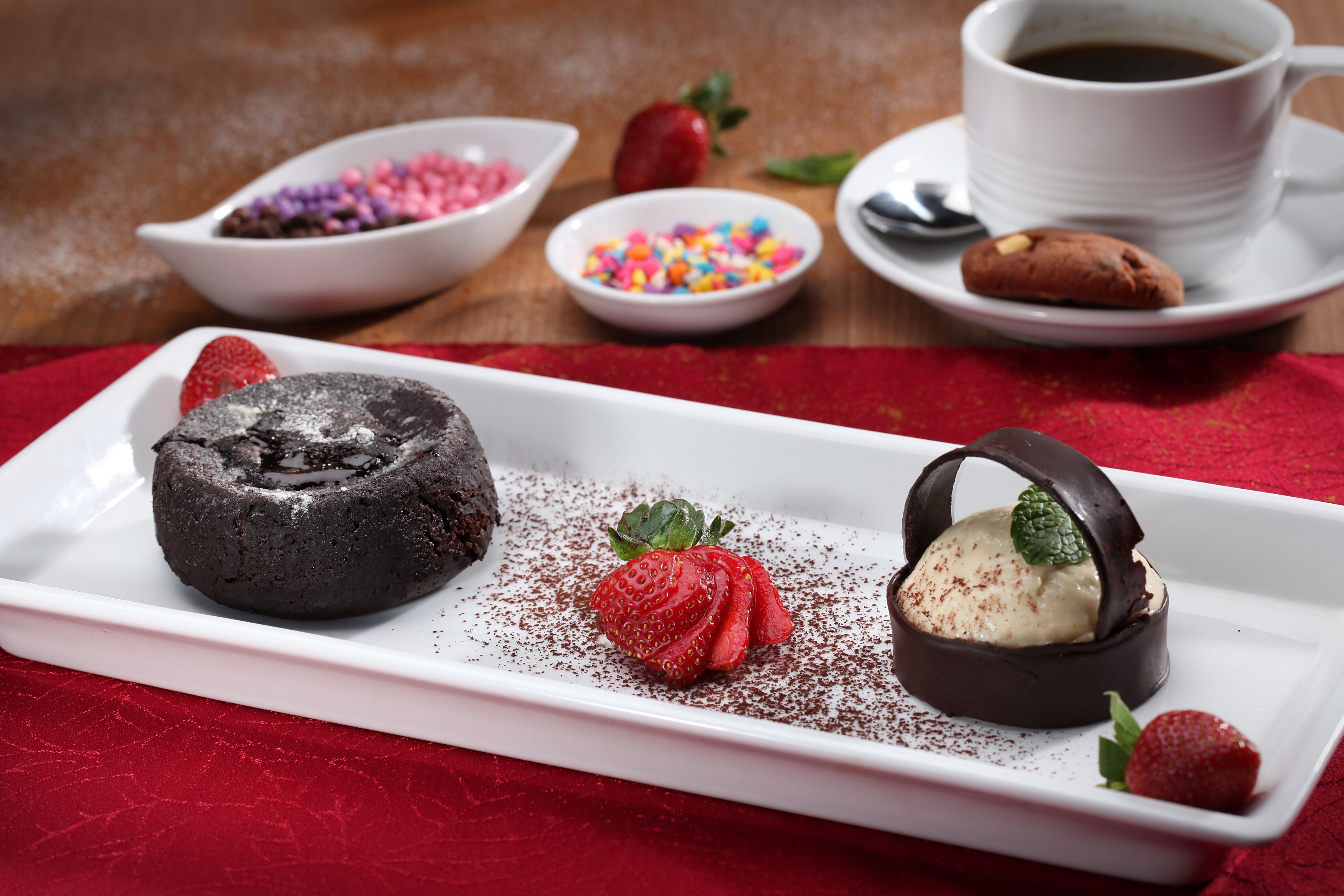 A dessert plate with a chocolate lava cake, a scoop of ice cream, and a strawberry on a red napkin.