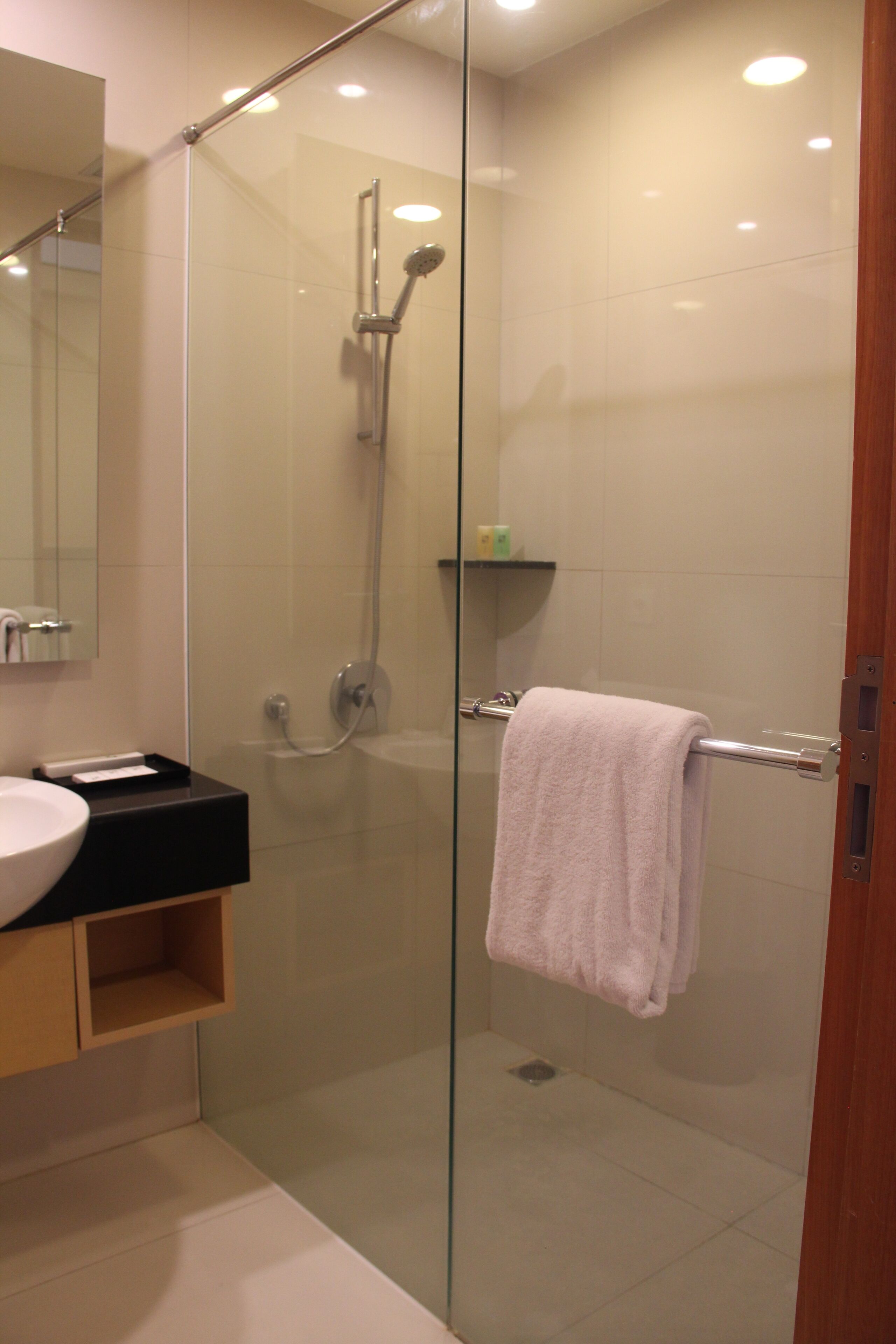 A modern bathroom with a glass-enclosed shower, a sink with a black countertop, and a wooden shelf.