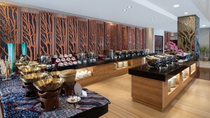 A buffet setup with various food items and serving ware, a decorative wall with a tree pattern, and a modern interior design. - Swiss-Belinn Manyar (Surabaya)