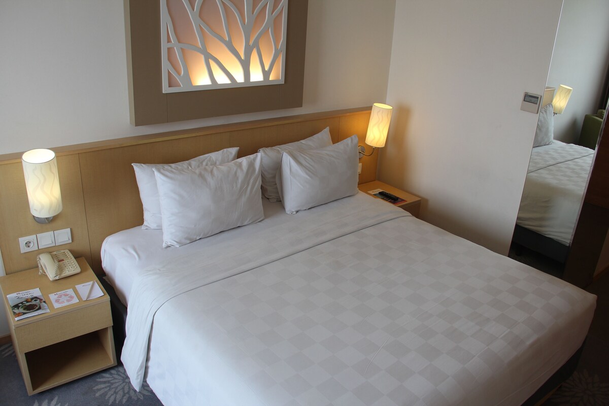 Ein Hotelzimmer mit einem Bett, zwei Nachttischlampen, einem Nachttisch mit Lampe, einer Wandleuchte und einem Spiegel.