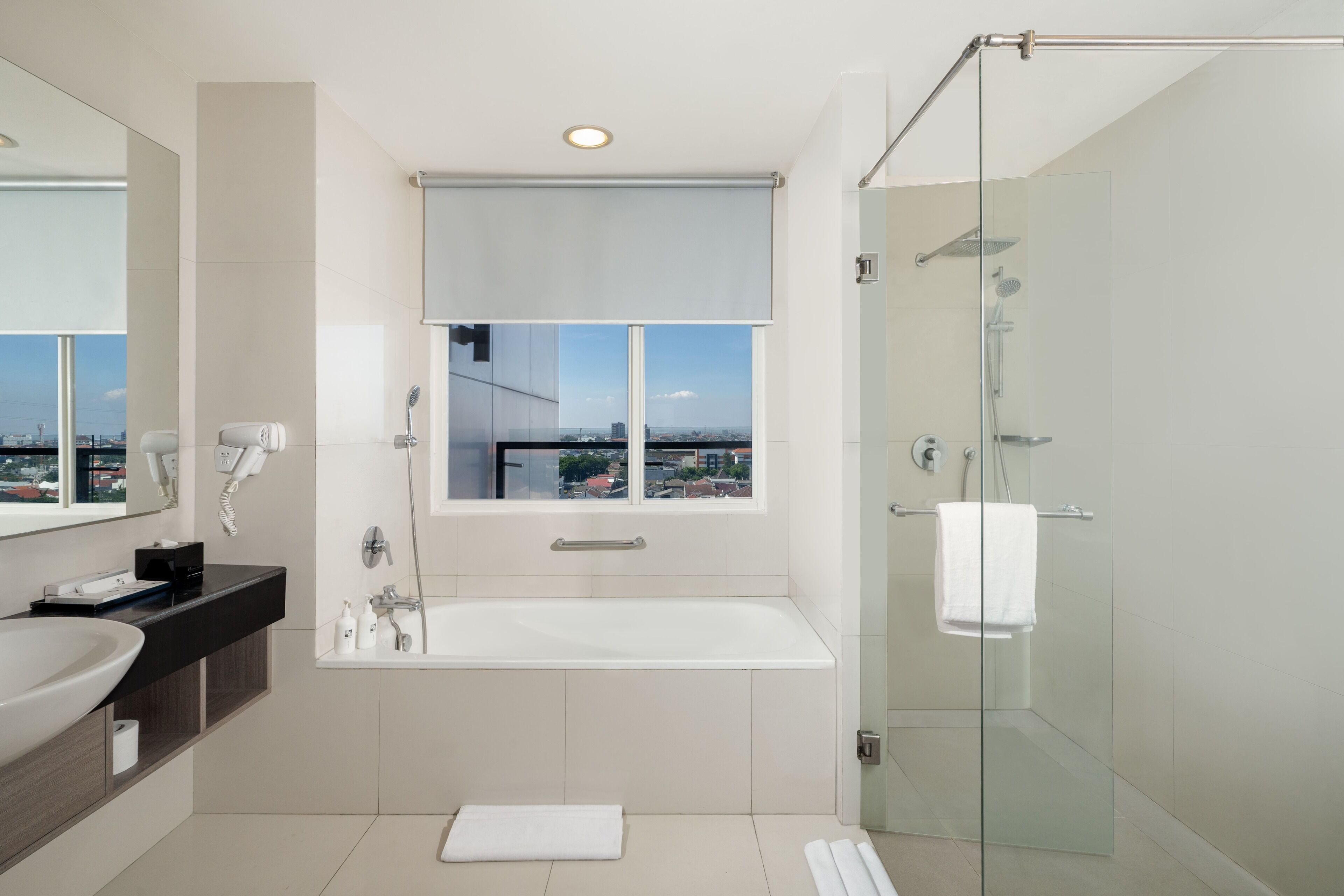 Een moderne badkamer met een groot bad, een glazen douchecabine, een wastafelmeubel en een raam met uitzicht op de stad.