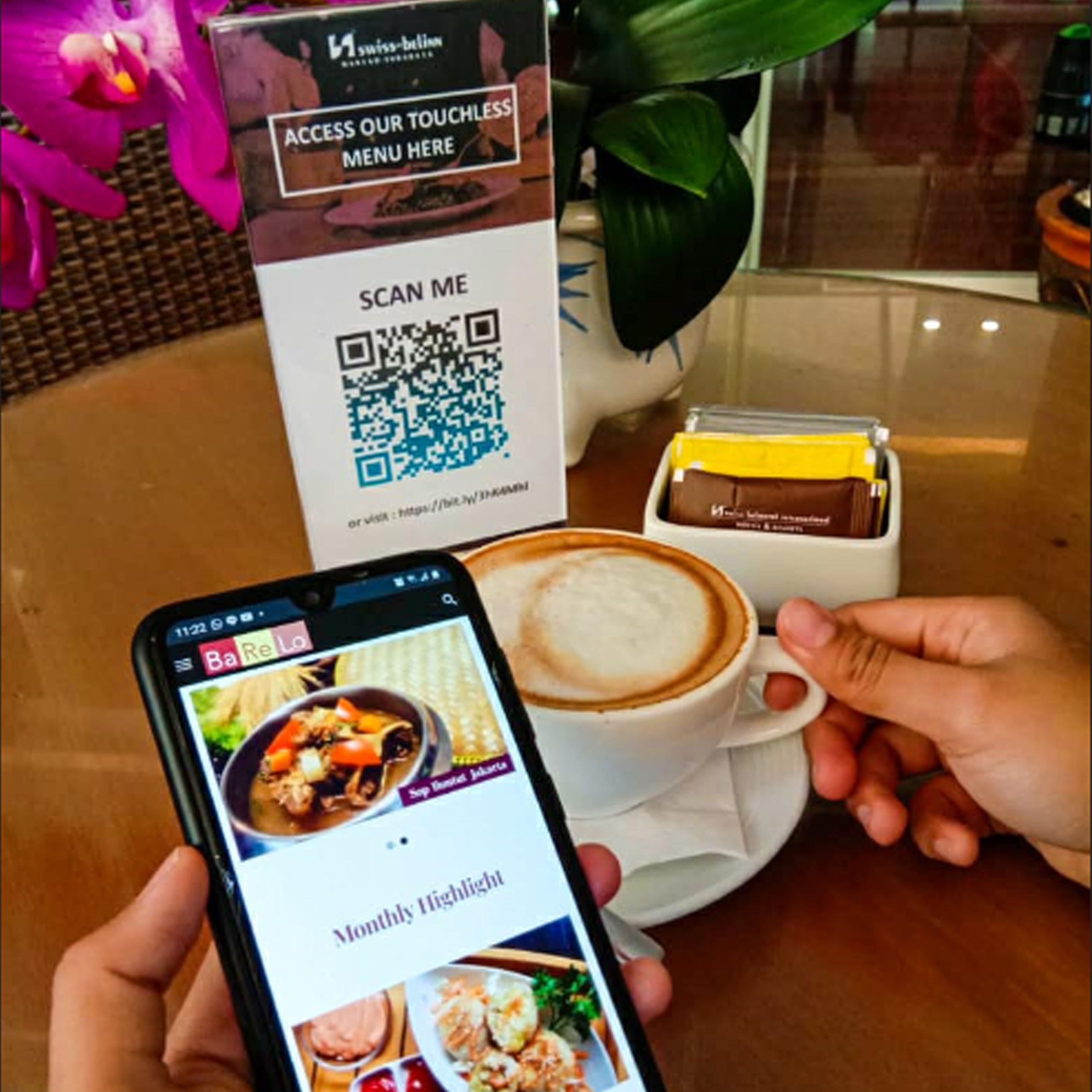 Un téléphone intelligent affichant le menu d’un restaurant, un code QR et une tasse de café sur une table.