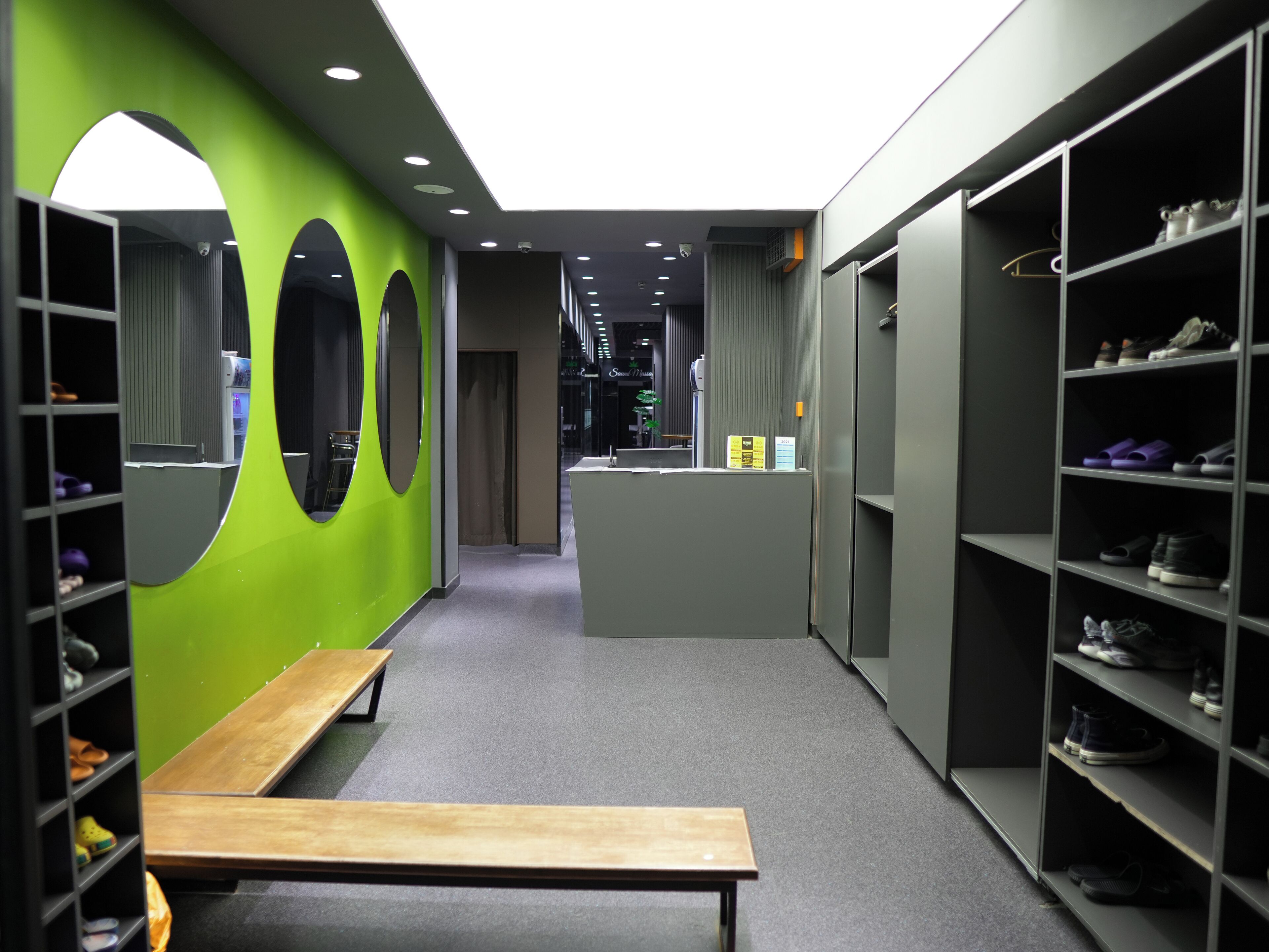 Un couloir aux murs verts, orné de miroirs ronds et doté d’étagères à chaussures.