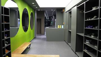 Un couloir aux murs verts, orné de miroirs ronds et doté d’étagères à chaussures.