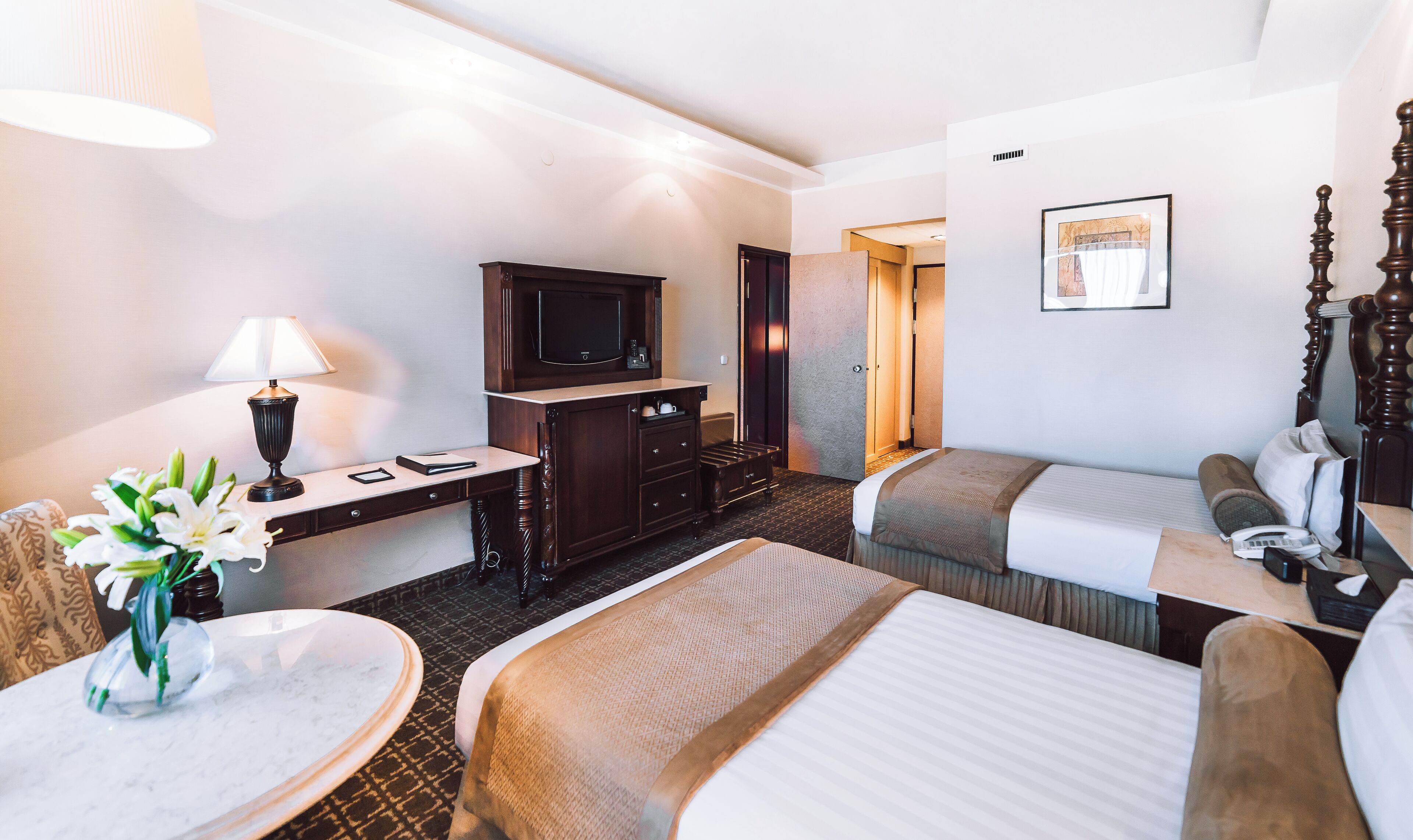 Ein Hotelzimmer mit zwei Betten, einem Schreibtisch mit Lampe, einem Fernseher und einem Badezimmer.