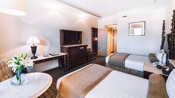 A hotel room with two beds, a desk with a lamp, a TV, and a bathroom.