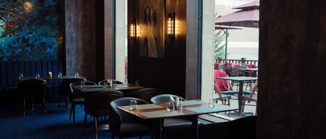 An indoor dining area with tables and chairs, a mural on the wall, and two wall-mounted lights.