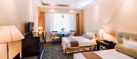 A hotel room with a bed, bedside tables, a desk with a TV, a chair, a small table with a plant, and a window with curtains.