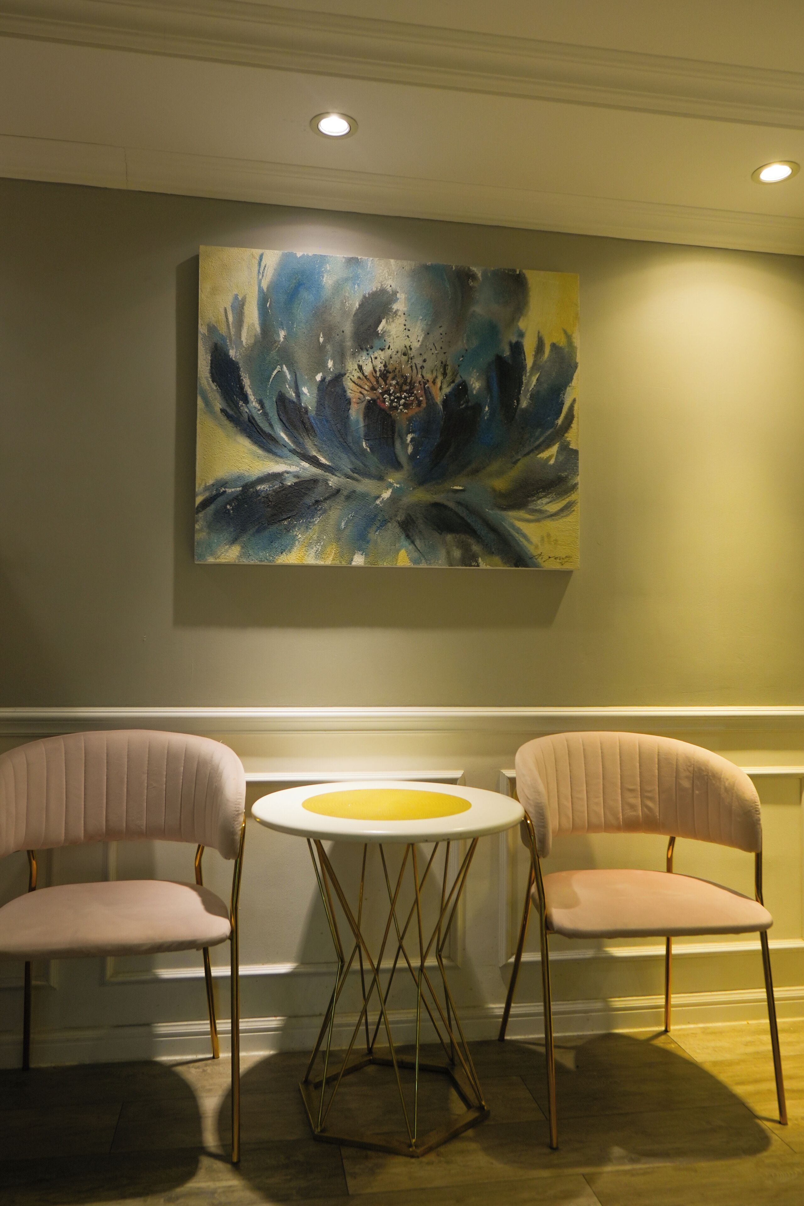 A room with two chairs and a table, a painting on the wall, and recessed ceiling lighting.