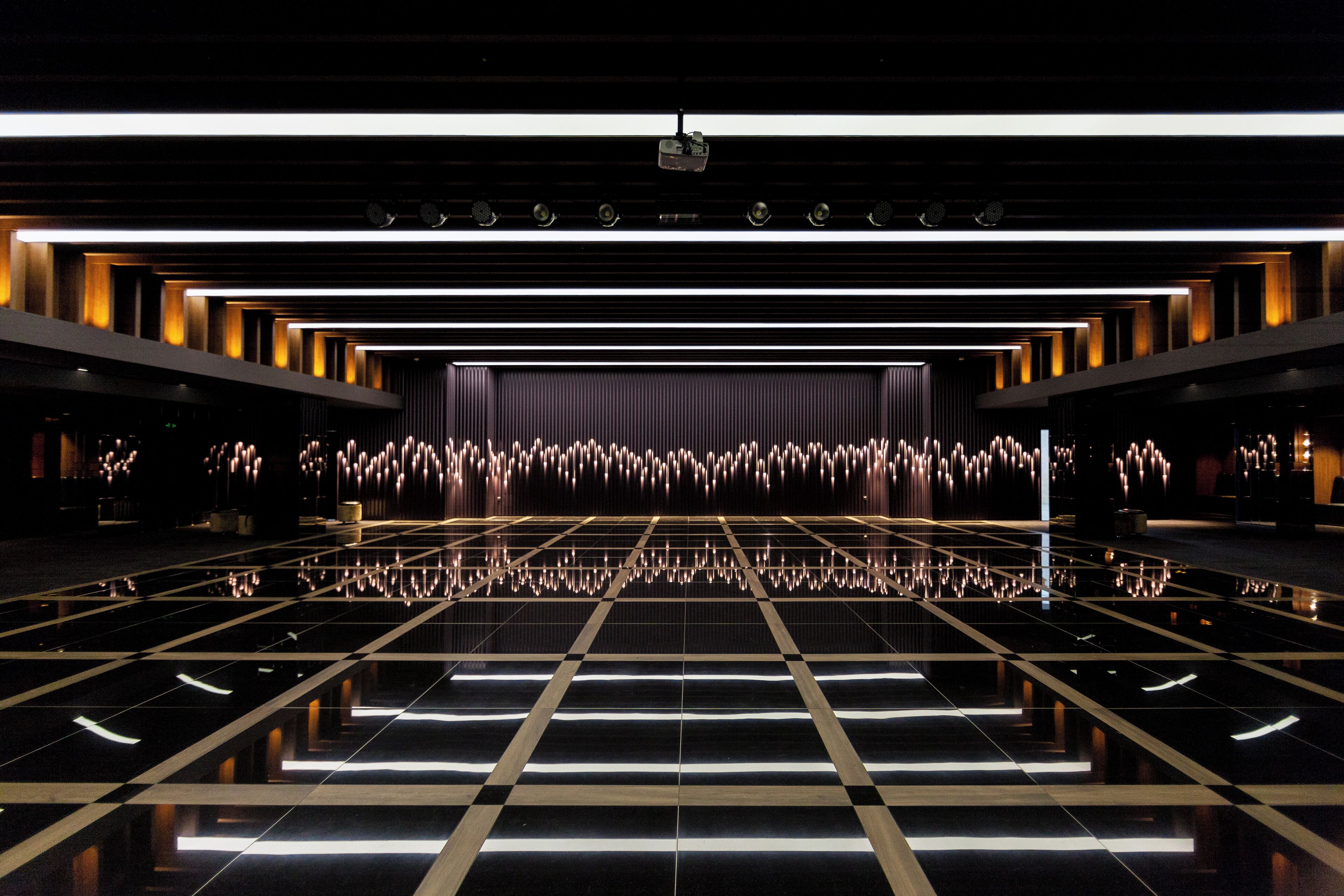 Un vestíbulo de hotel moderno con piso reflectante, un escenario con telón de fondo y una fila de asientos a cada lado.